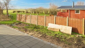 A paved walkway leading to a fenced area with a red building and a chimney. - 4 Star Holiday Home in Gorlev (Gørlev)