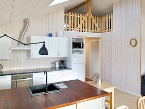 A compact kitchen with white cabinets, a wooden dining table, a black desk lamp, and a microwave. - 4 Star Holiday Home in Gorlev (Gørlev)