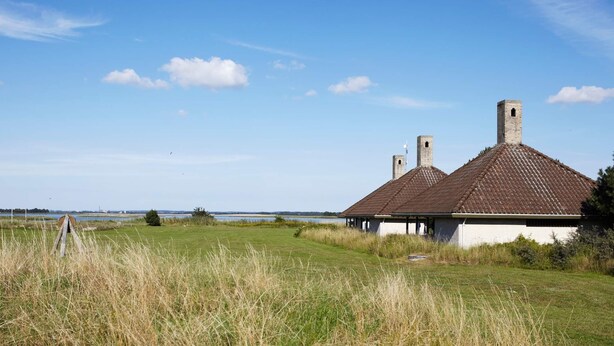 A traditional building with a tiled roof and chimneys, situated in a grassy field with a clear sky and distant water body. - 5 Person Holiday Home on a Holiday Park in Karrebaeksminde (Karrebæksminde)