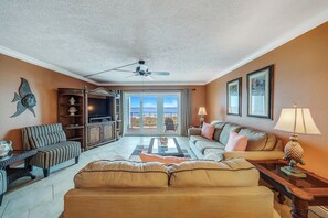 A spacious living room with a large television, comfortable seating, and a view of the outdoors.