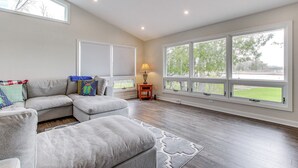 A spacious living room with a sectional sofa, a rug, and large windows offering a view of the outdoors.