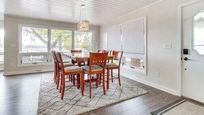 A dining area with a wooden table and chairs, large windows, and a ceiling with exposed beams.
