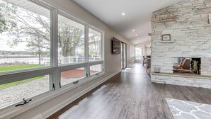 A spacious room with large windows, a stone fireplace, and a view of a lake.