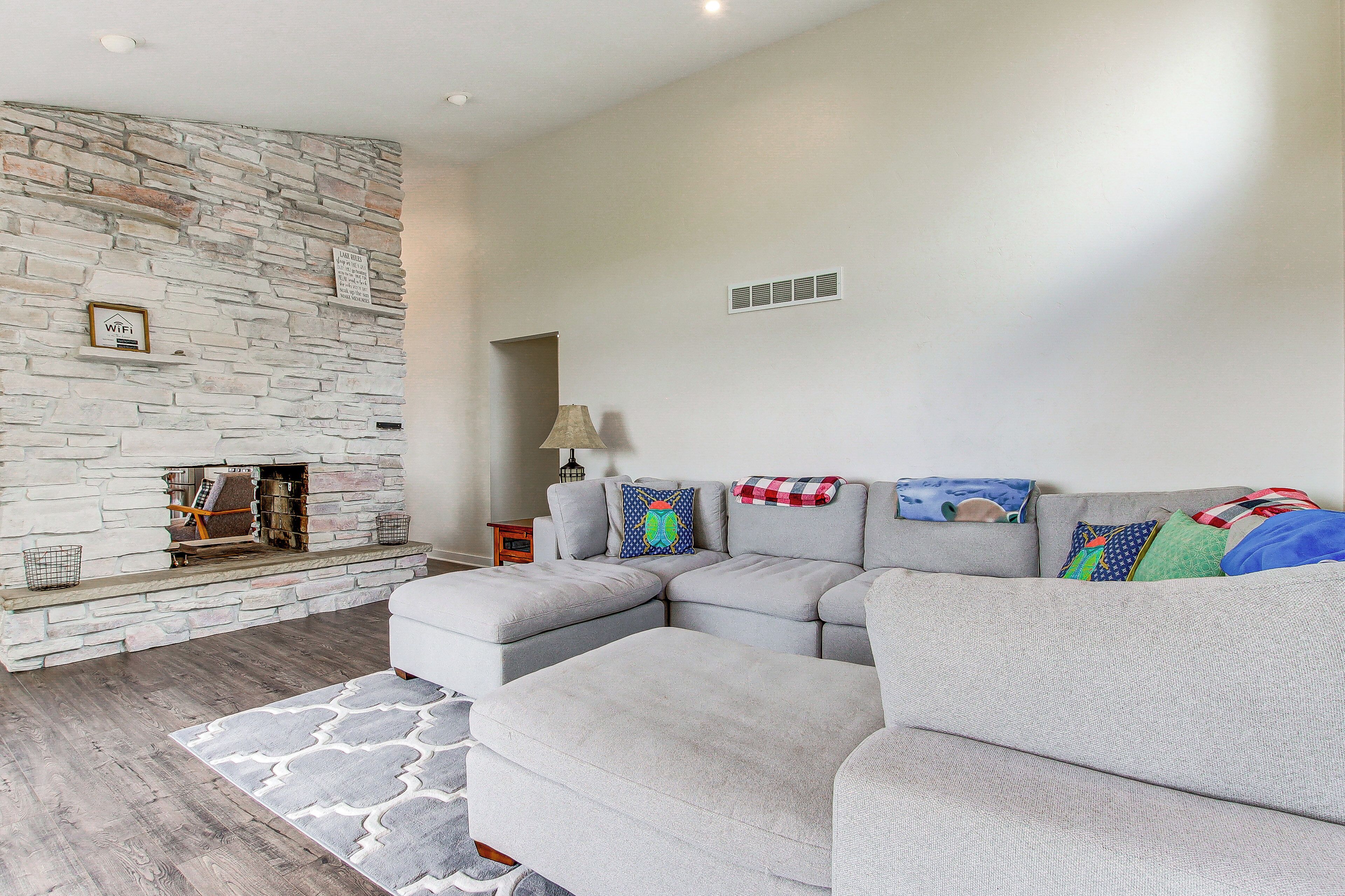 A modern living room with a stone fireplace, grey sectional sofa, and a patterned rug.