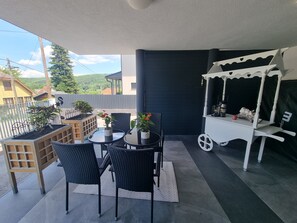 A balcony with a table and chairs, a white cart with a coffee machine, and potted plants. - Luxury Vienna  (Mauerbach)