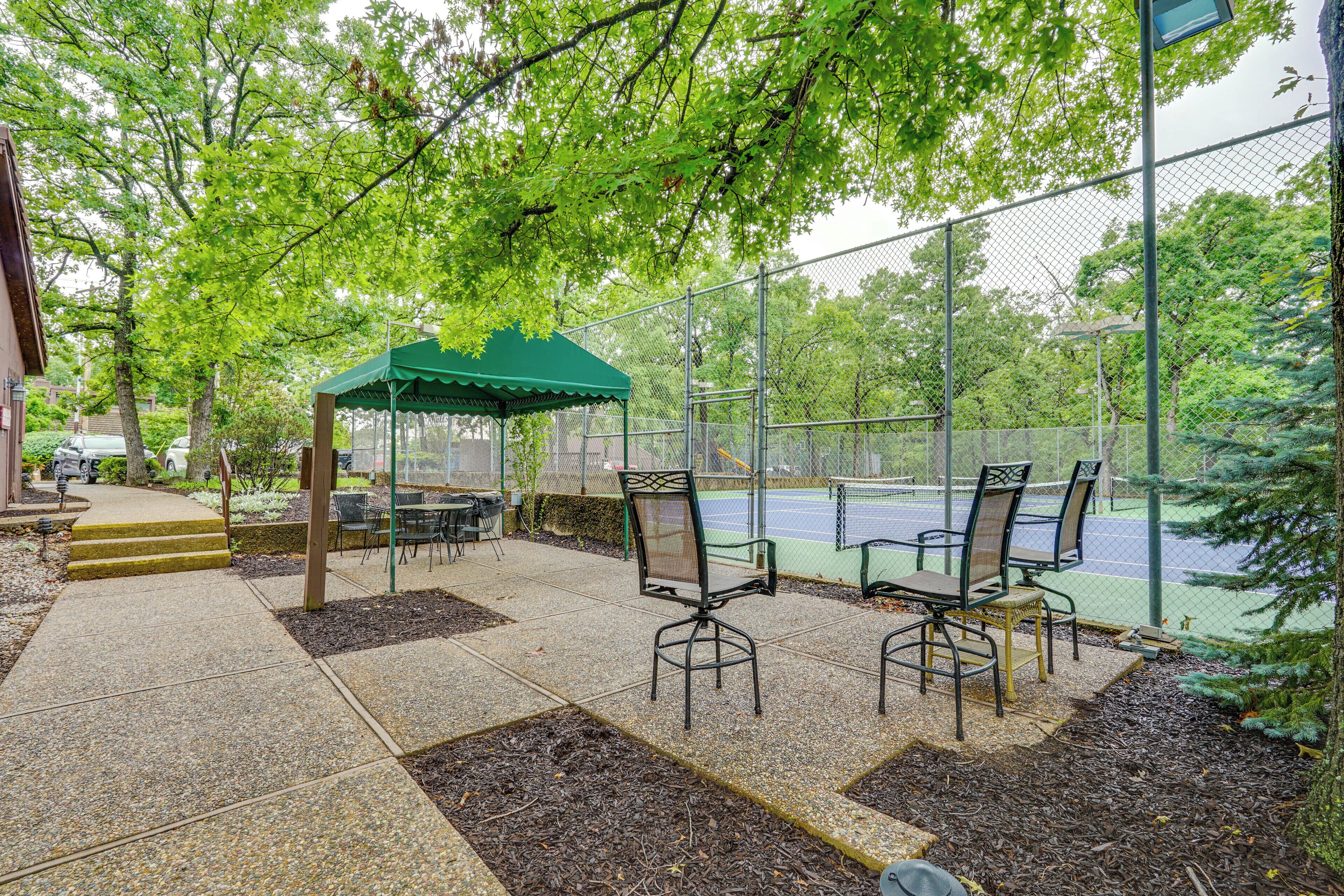Un espace extérieur aménagé avec un coin salon, une pergola couverte de verdure, un court de tennis et une aire de jeux clôturée.
