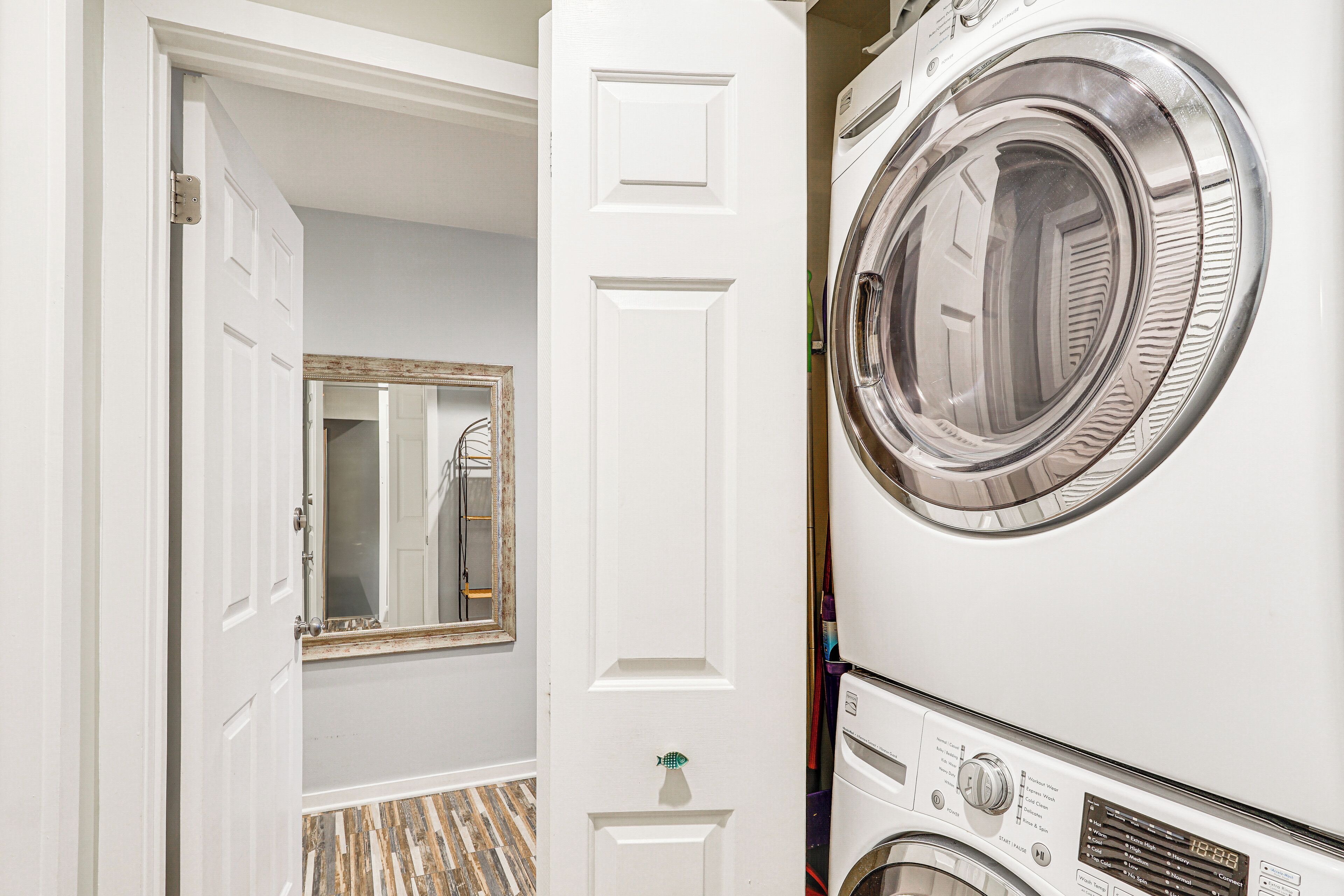 A laundry room with a front-loading washer and dryer, a mirror, and a door leading to another room.