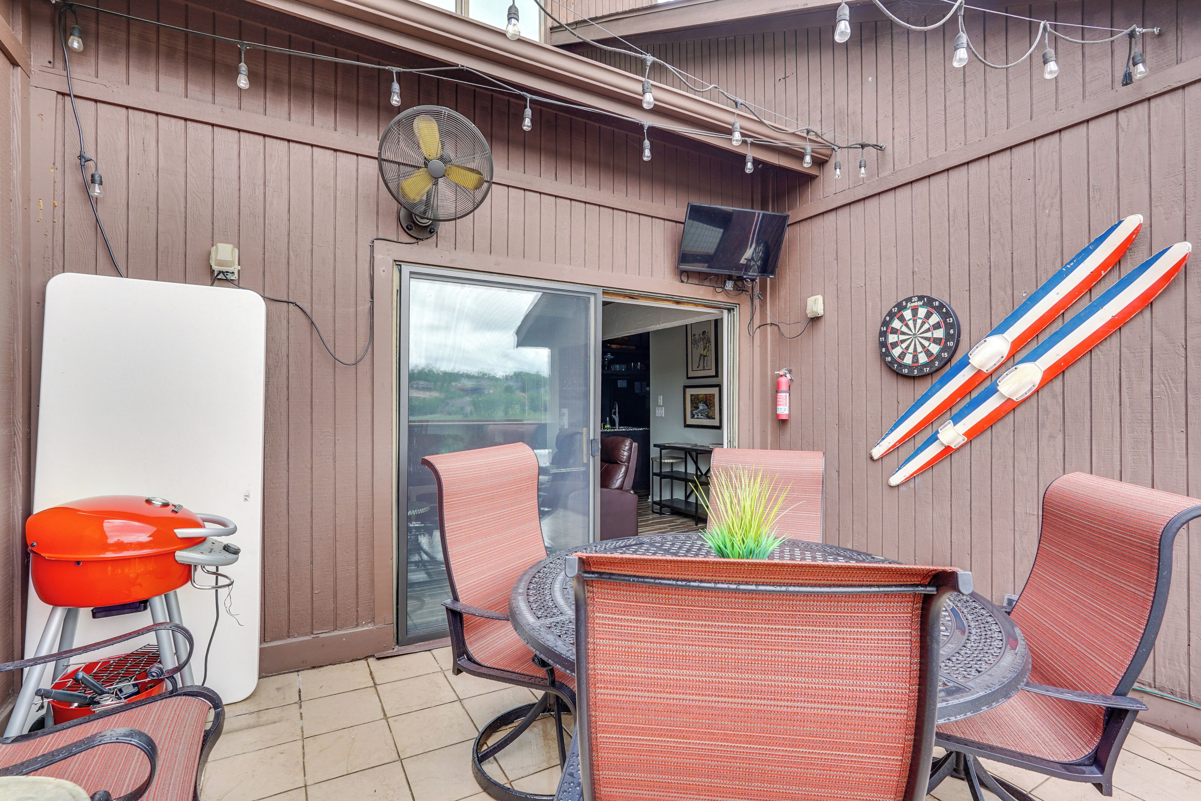 An outdoor patio with wicker chairs, a table with a plant, a barbecue grill, and a dartboard.