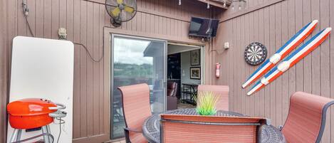 An outdoor patio with wicker chairs, a table with a plant, a barbecue grill, and a dartboard.