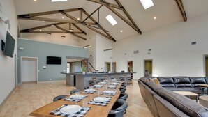 Un vaste espace dédié à la salle à manger, avec une longue table en bois dressée pour le repas, un canapé en cuir et, au fond, une cuisine.