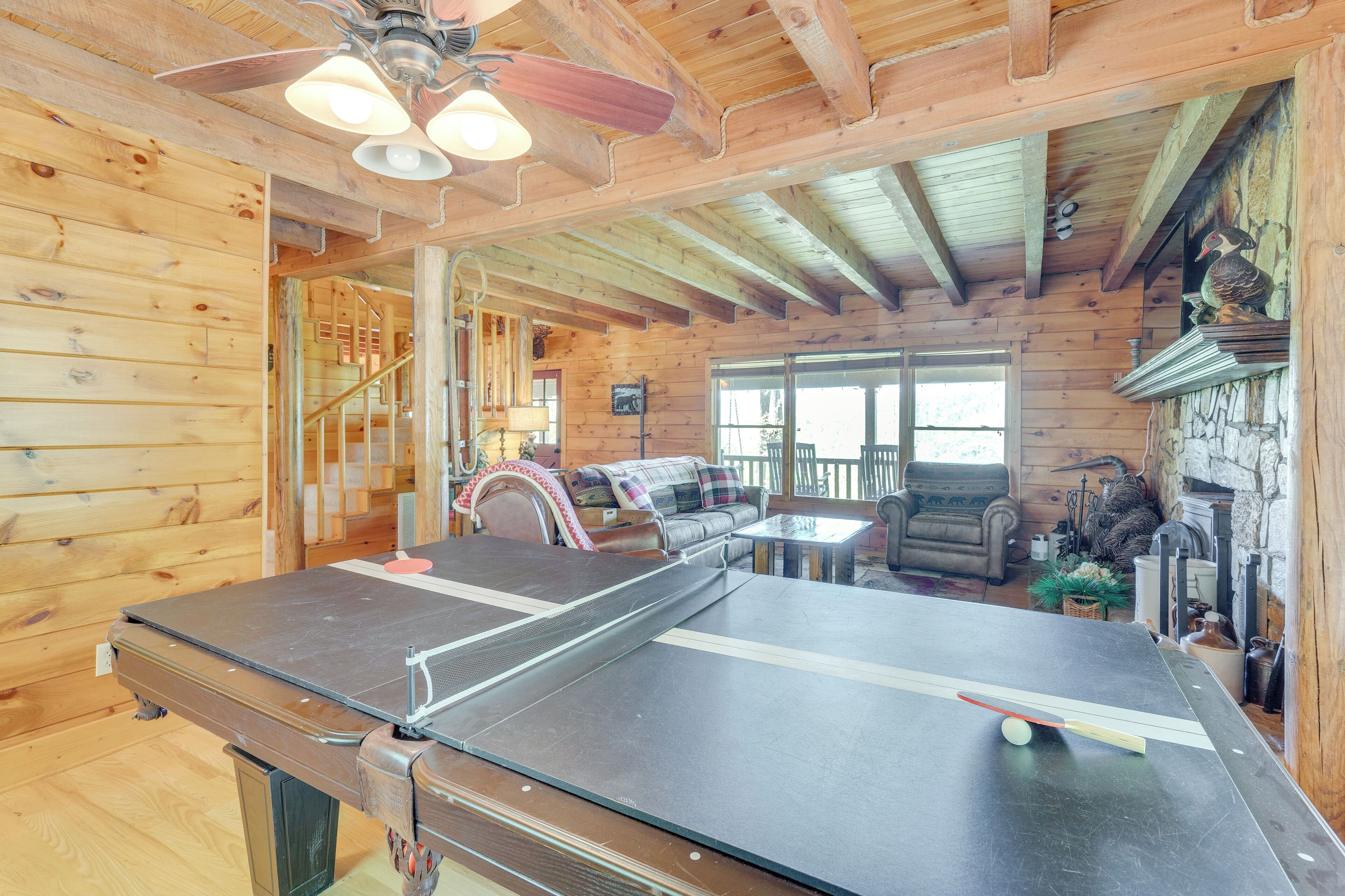 A wooden cabin interior with a ping pong table, a staircase, a fireplace, and a cozy seating area.