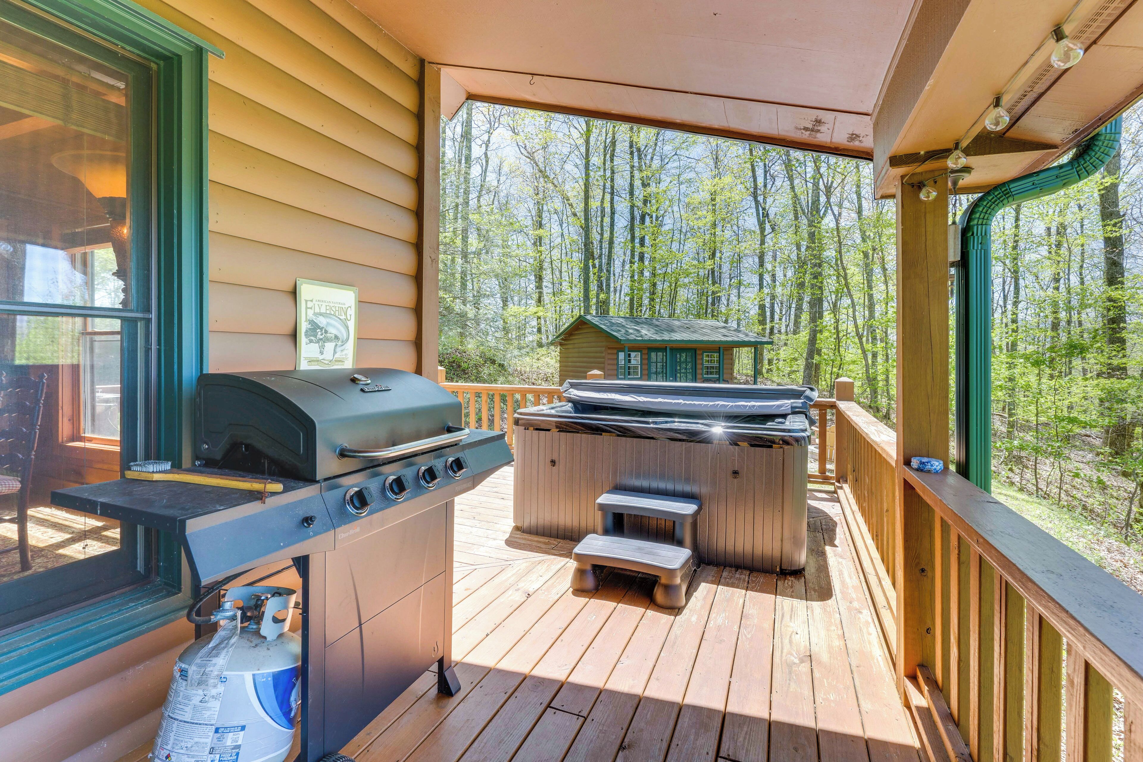 A covered outdoor deck with a grill, hot tub, and a view of a forest.