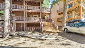 A multi-story wooden building with a central staircase, a car parked nearby, and a surrounding area with trees and gravel. - Easy Resort Access: Angel Fire Adventure Condo! (Angel Fire)