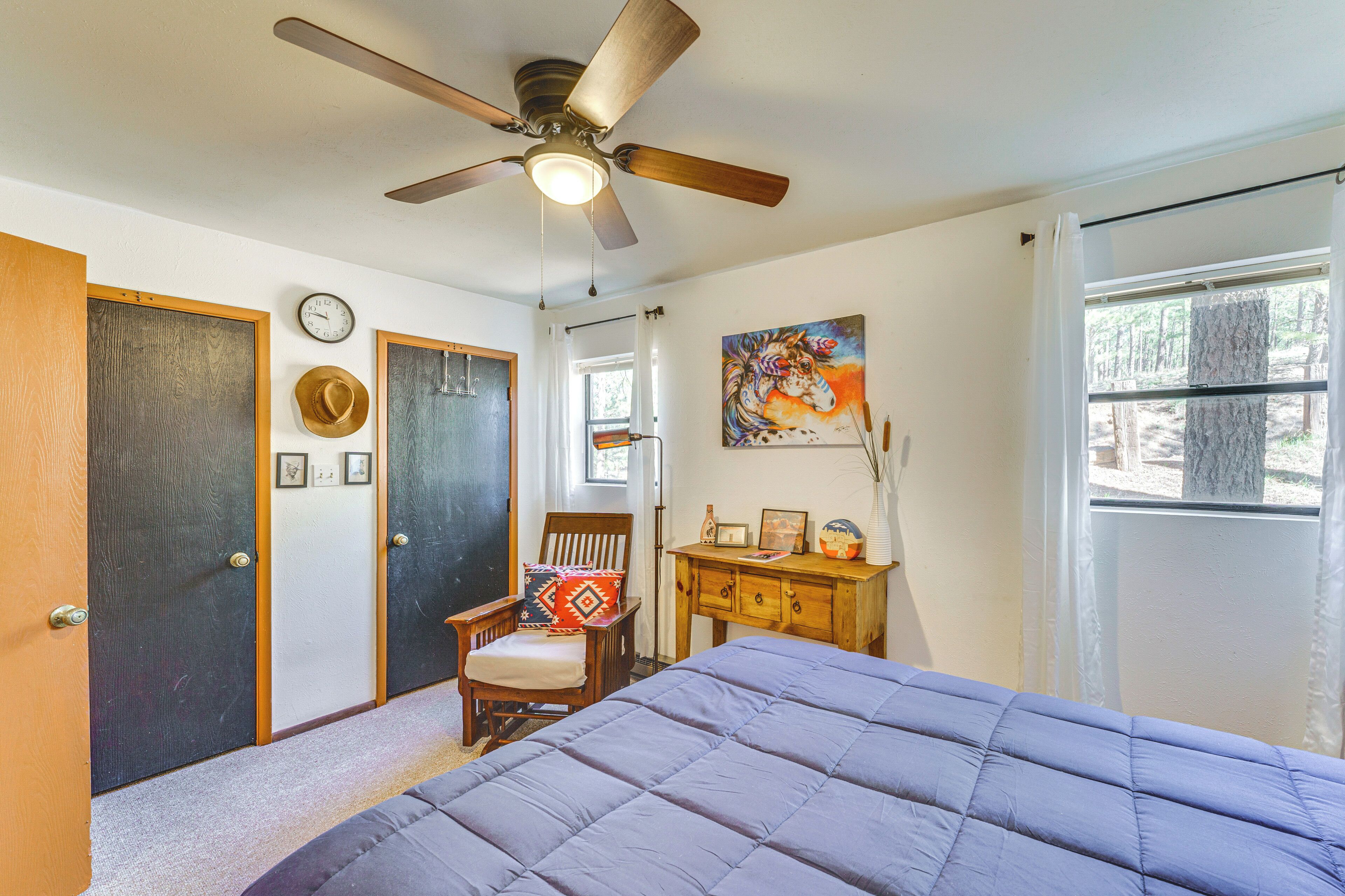 A bedroom with a bed, a ceiling fan, a chair, a dresser, a painting, and a window.