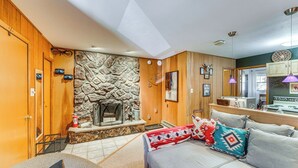A cozy living room with a stone fireplace, wooden walls, and a sofa with patterned cushions. - Easy Resort Access: Angel Fire Adventure Condo! (Angel Fire)