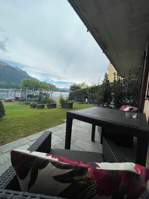 Eine Terrasse im Freien mit Tisch und Stühlen, einer Rasenfläche und Blick auf einen See und Berge.