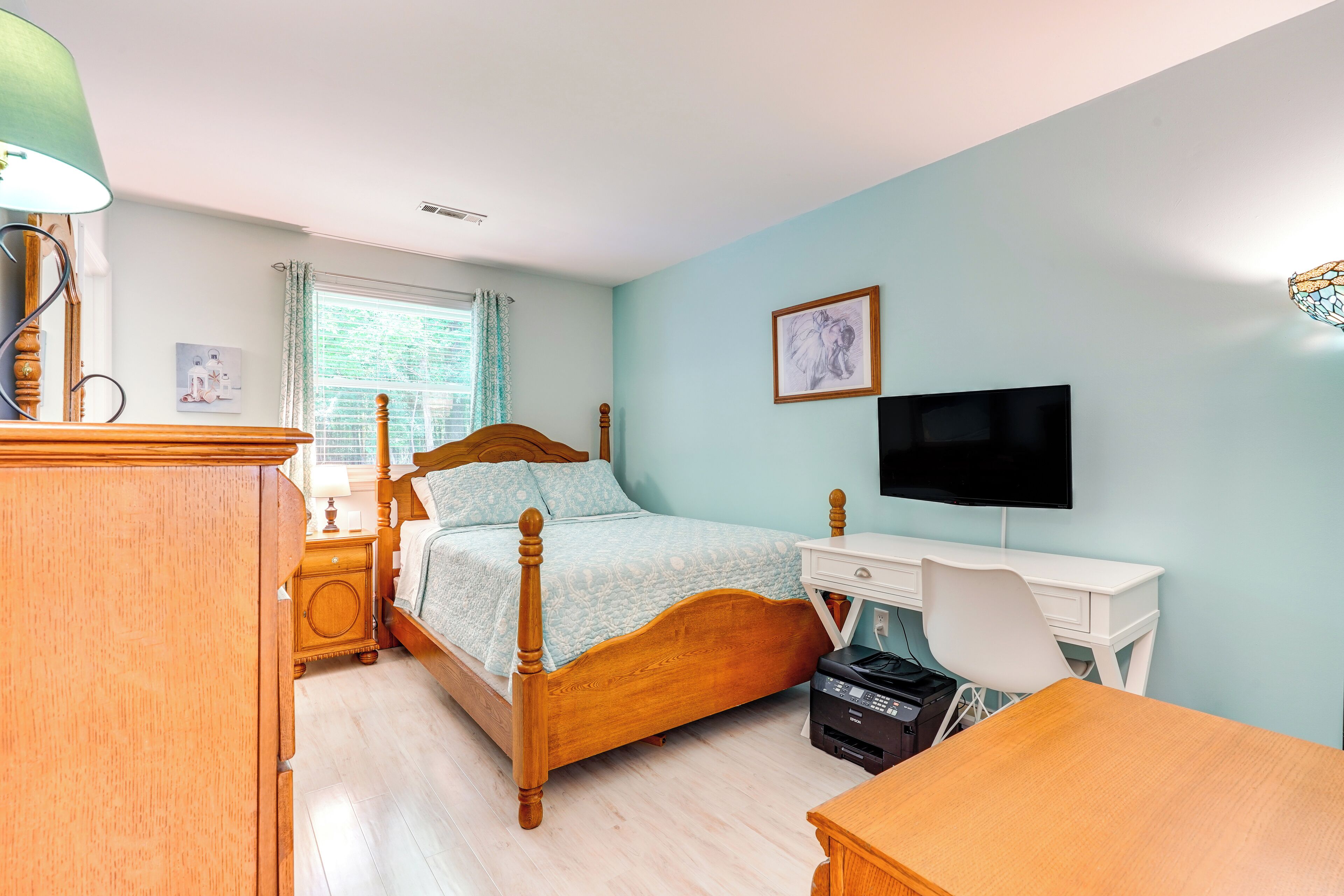 Une chambre à coucher avec un lit en bois, un bureau, une chaise, un téléviseur et une fenêtre avec des rideaux.