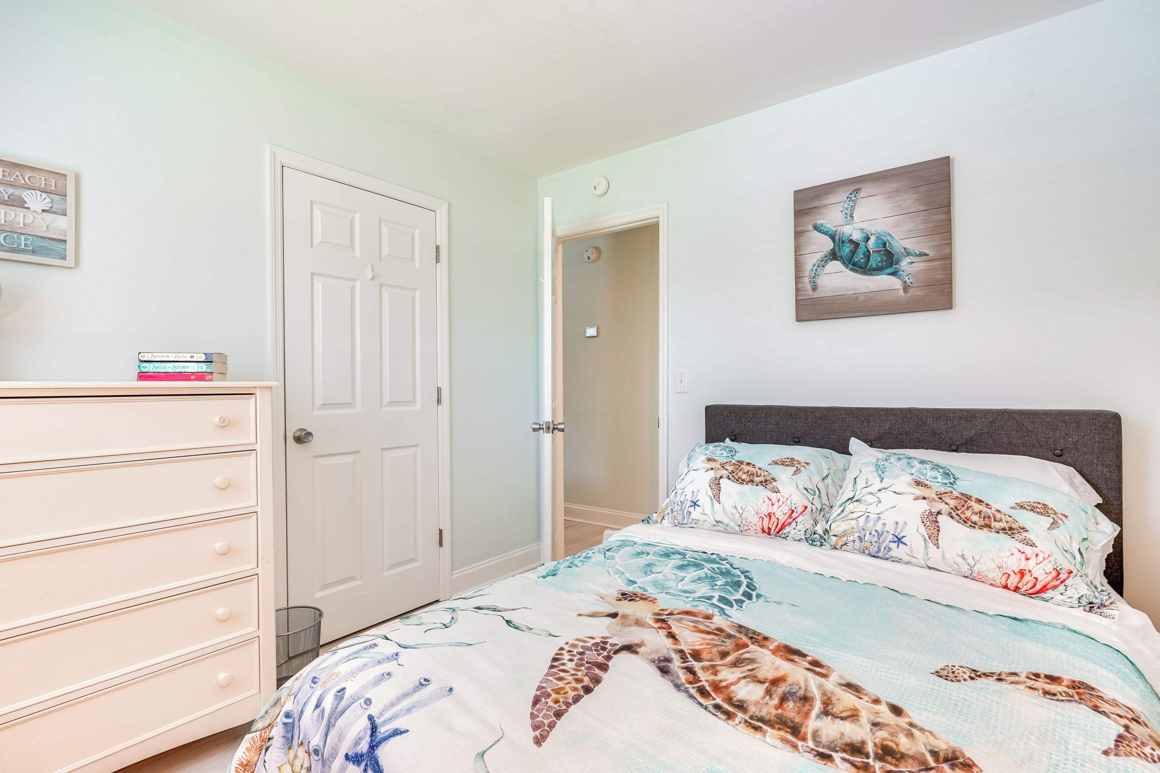 A bedroom with a bed featuring a sea turtle print, a dresser, and a door.