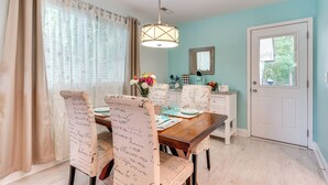 Un comedor con una mesa de madera, sillas con notas escritas a mano, una lámpara colgante y una puerta blanca con ventana.