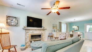 Una sala de estar con chimenea, ventilador de techo, televisor y sofá azul claro.