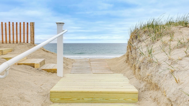 A wooden staircase leading to a beach with a wooden fence on one side and a white railing on the other.