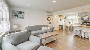 A modern living room with a grey sofa, a wooden coffee table, and a dining area with a kitchen in the background.