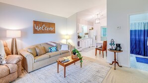 A living room with a sofa, coffee table, and a 'Welcome' sign. There is a kitchen in the background with white cabinets and a dining area. - Roanoke Mountain Home: 4 Mi to Blue Ridge Parkway! (Roanoke)