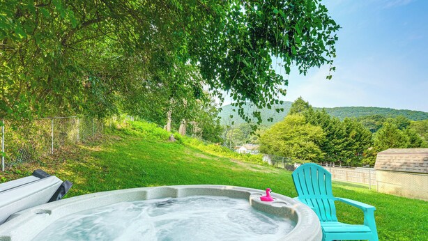 A hot tub with a pink flamingo toy, a turquoise Adirondack chair, and a grassy area with trees and hills in the background. - Roanoke Mountain Home: 4 Mi to Blue Ridge Parkway! (Roanoke)