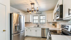 Une cuisine moderne dotée d’appareils électroménagers en acier inoxydable, de meubles blancs, d’un îlot central et d’un luminaire au plafond.