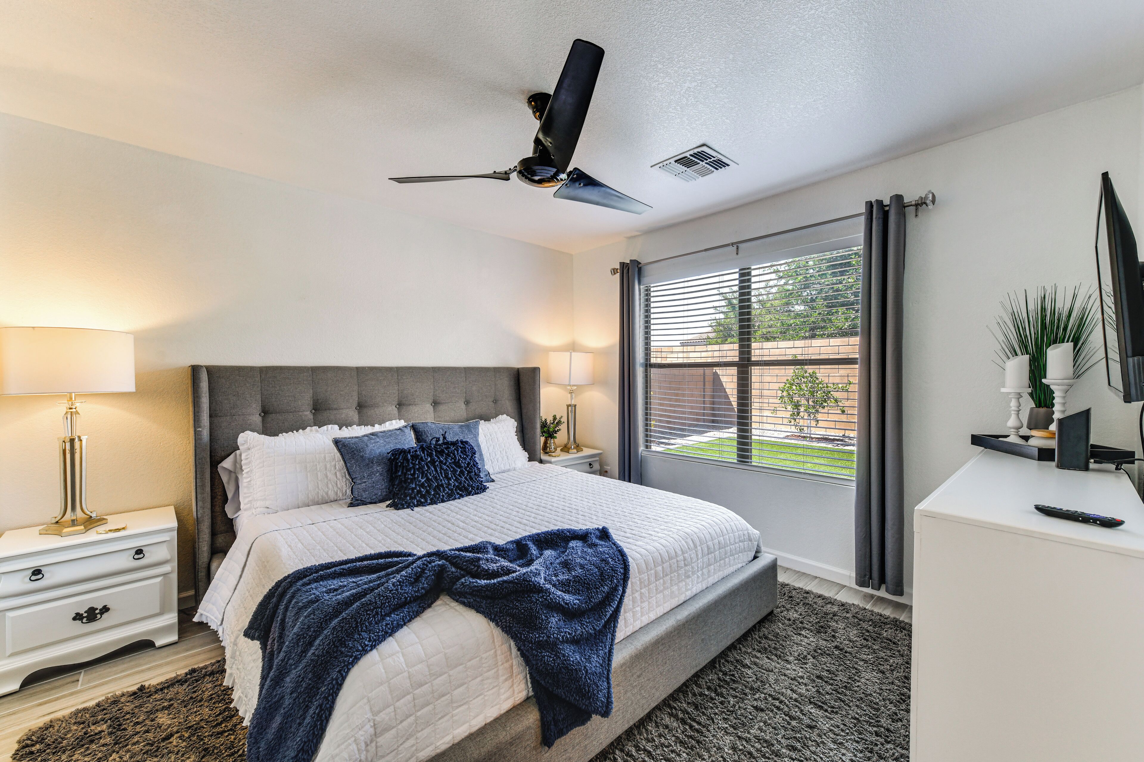 A bedroom with a bed, nightstands, a desk, a ceiling fan, and a window with curtains.