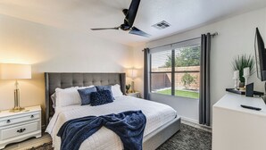 Une chambre à coucher comprenant un lit, des tables de chevet, un bureau, un ventilateur de plafond et une fenêtre avec des rideaux.