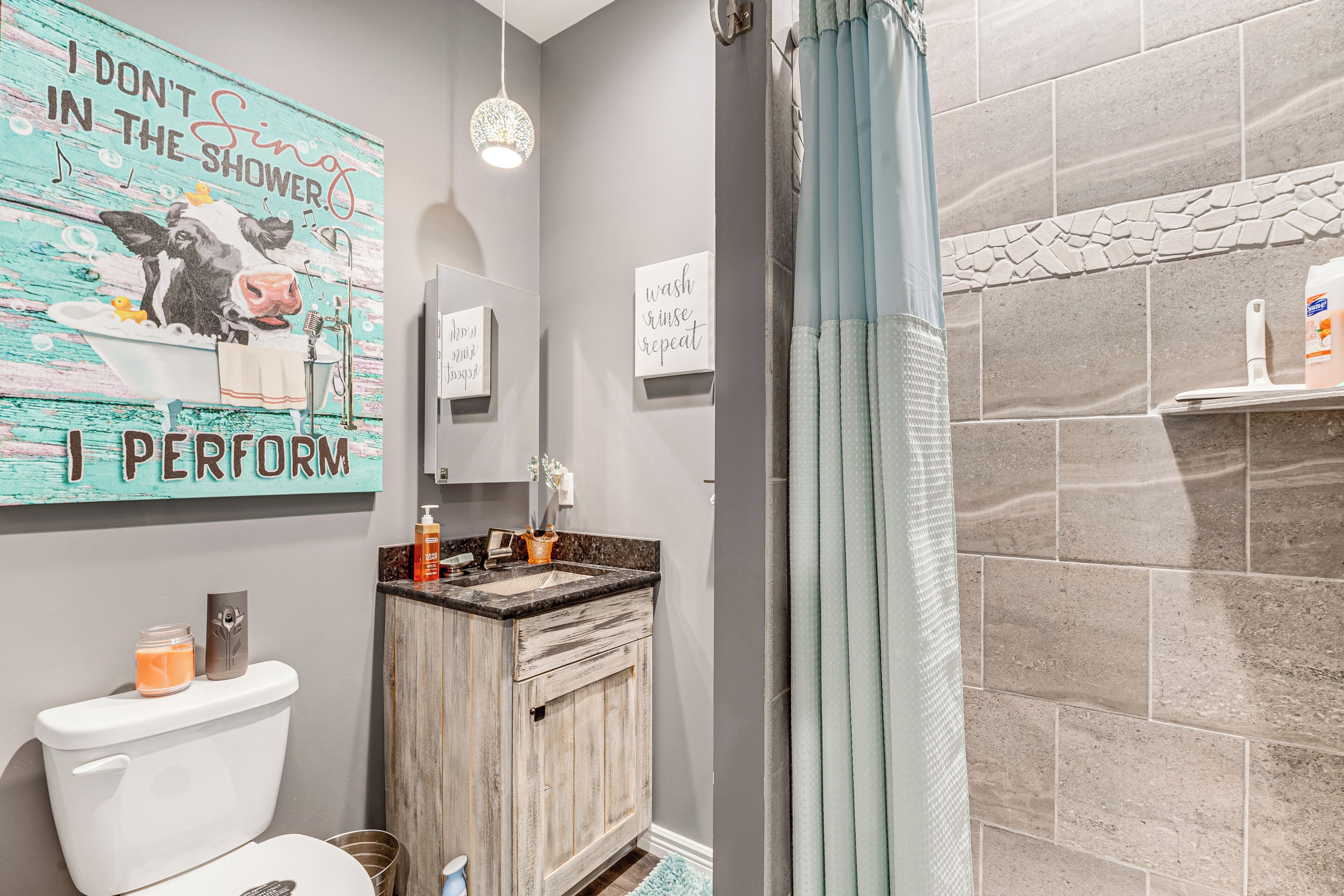 A bathroom with a toilet, a sink, a shower, and a decorative wall with a cow illustration and text.