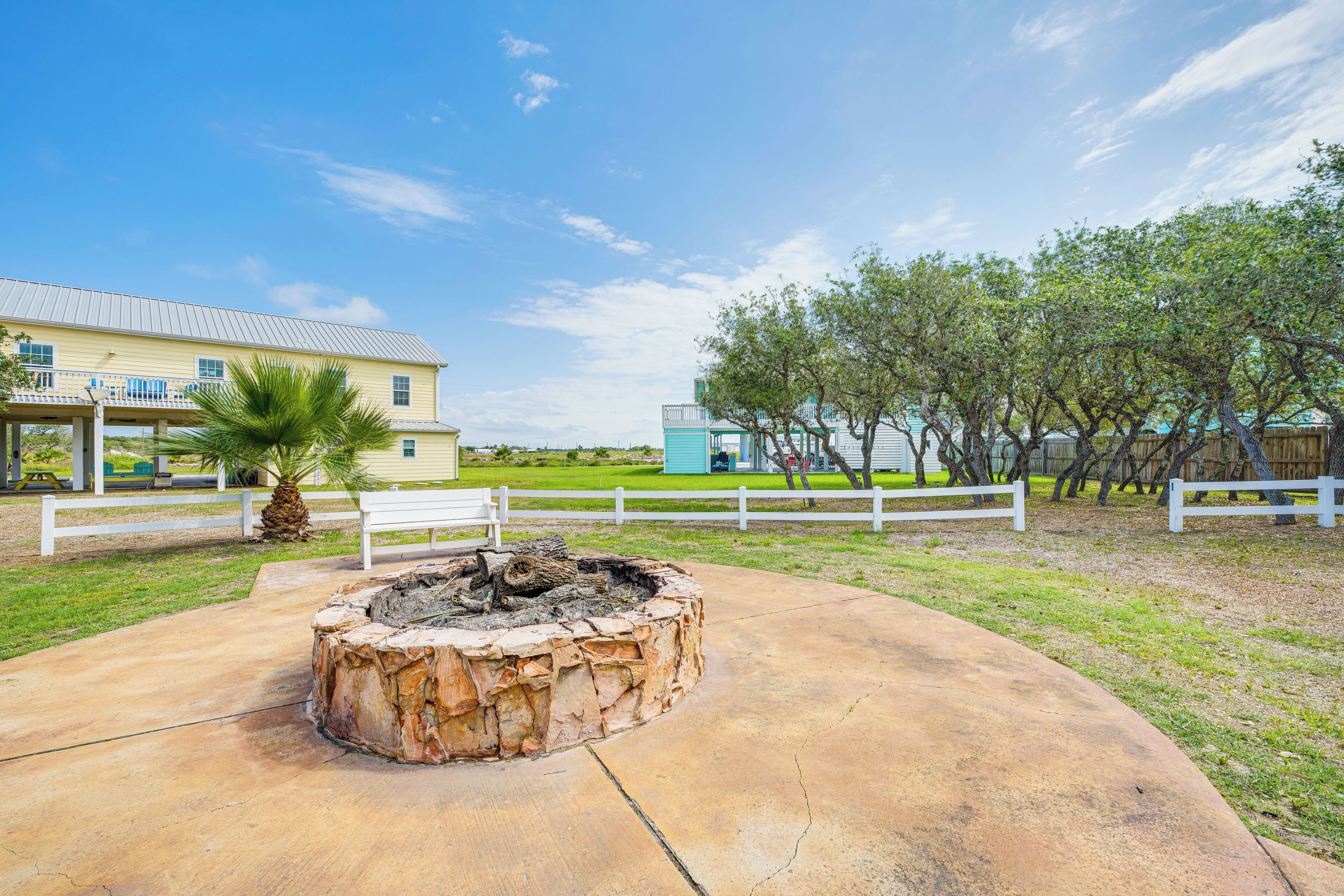 A concrete patio with a fire pit, white fences, and a building with a blue roof in the background.
