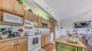 A kitchen with wooden cabinets, a microwave, a stove, and a dining table with a green chair. - Alto Townhome w/ Deck Near Ski Apache! (Alto)