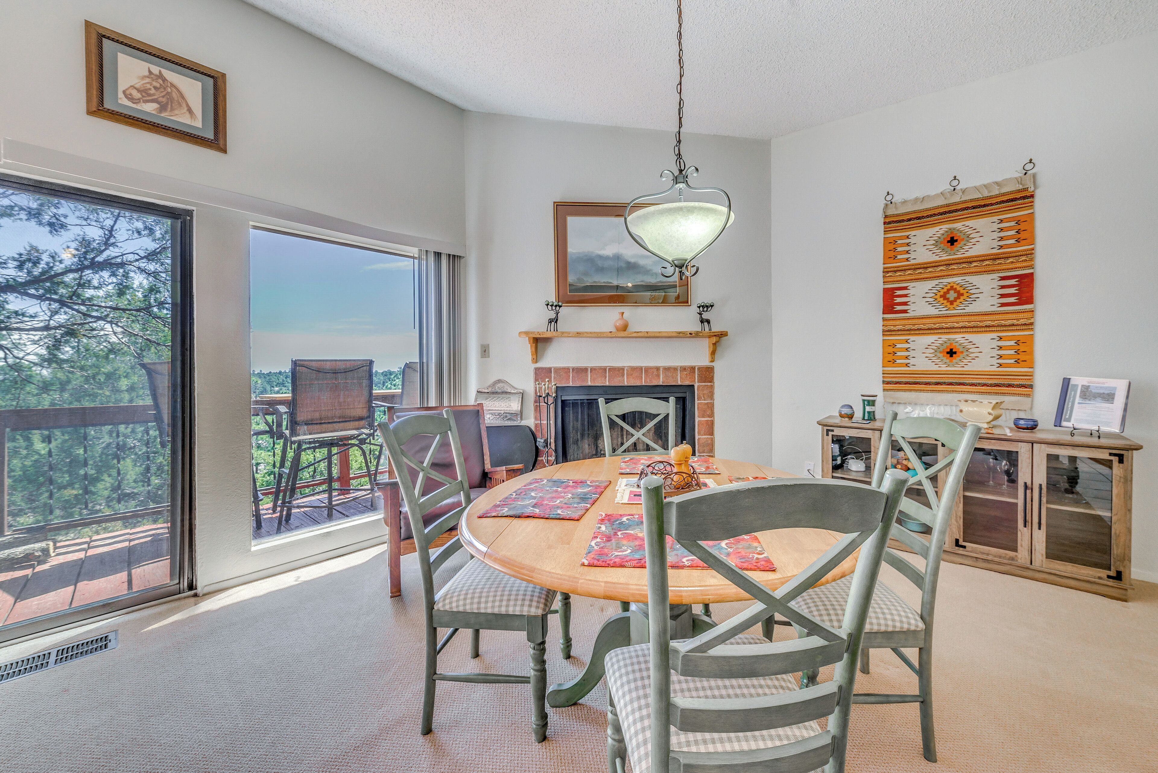 A dining area with a round table, chairs, a hanging light fixture, and a fireplace.