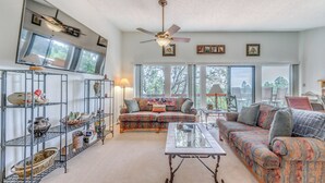 A spacious living room with a large sofa, a coffee table, and a ceiling fan. There are shelves with decorative items and a large window providing natural light. - Alto Townhome w/ Deck Near Ski Apache! (Alto)