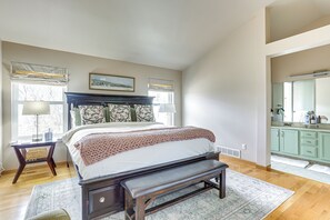 Relax in this serene bedroom with a large bed, a comfortable bench, and a peaceful view of the surrounding trees.