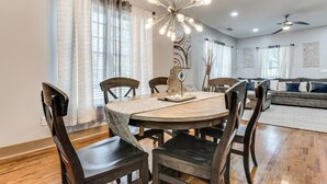 A dining area with a round table, wooden chairs, a chandelier, and a sofa in the background. - Unbeatable Hub 1 Mi to Mercedes-benz Stadium, Dtwn (Atlanta)