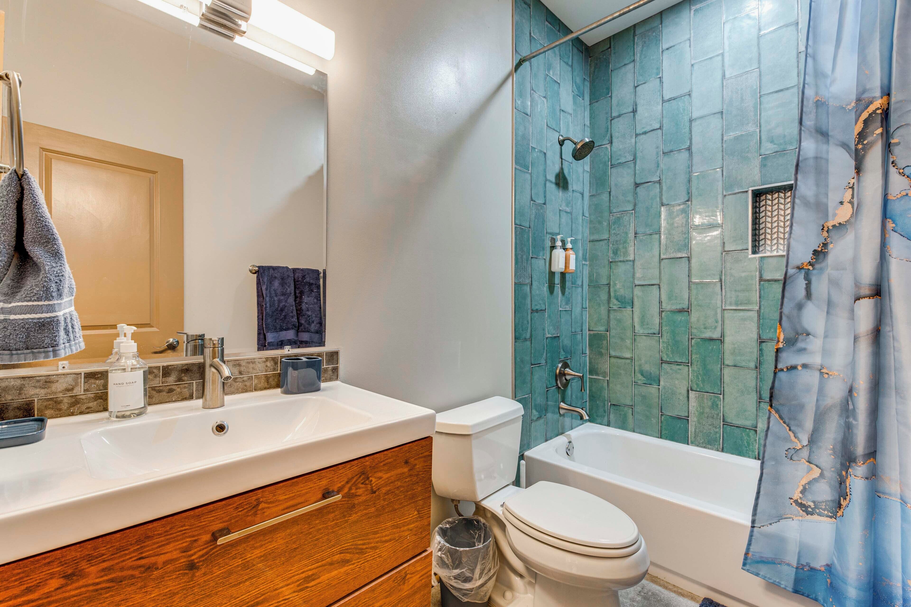 A bathroom with a white sink, wooden vanity, a toilet, and a shower with blue tiles.