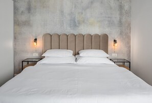 Un lit double avec une tête de lit rembourrée, deux tables de chevet avec des lampes et un mur à motifs en arrière-plan.