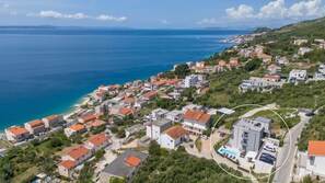 Vue aérienne d’une zone résidentielle côtière, avec des maisons, une plage et une vaste étendue d’eau.