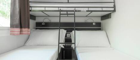 A bunk bed room with two beds, a ladder, a small table, and a window with curtains.
