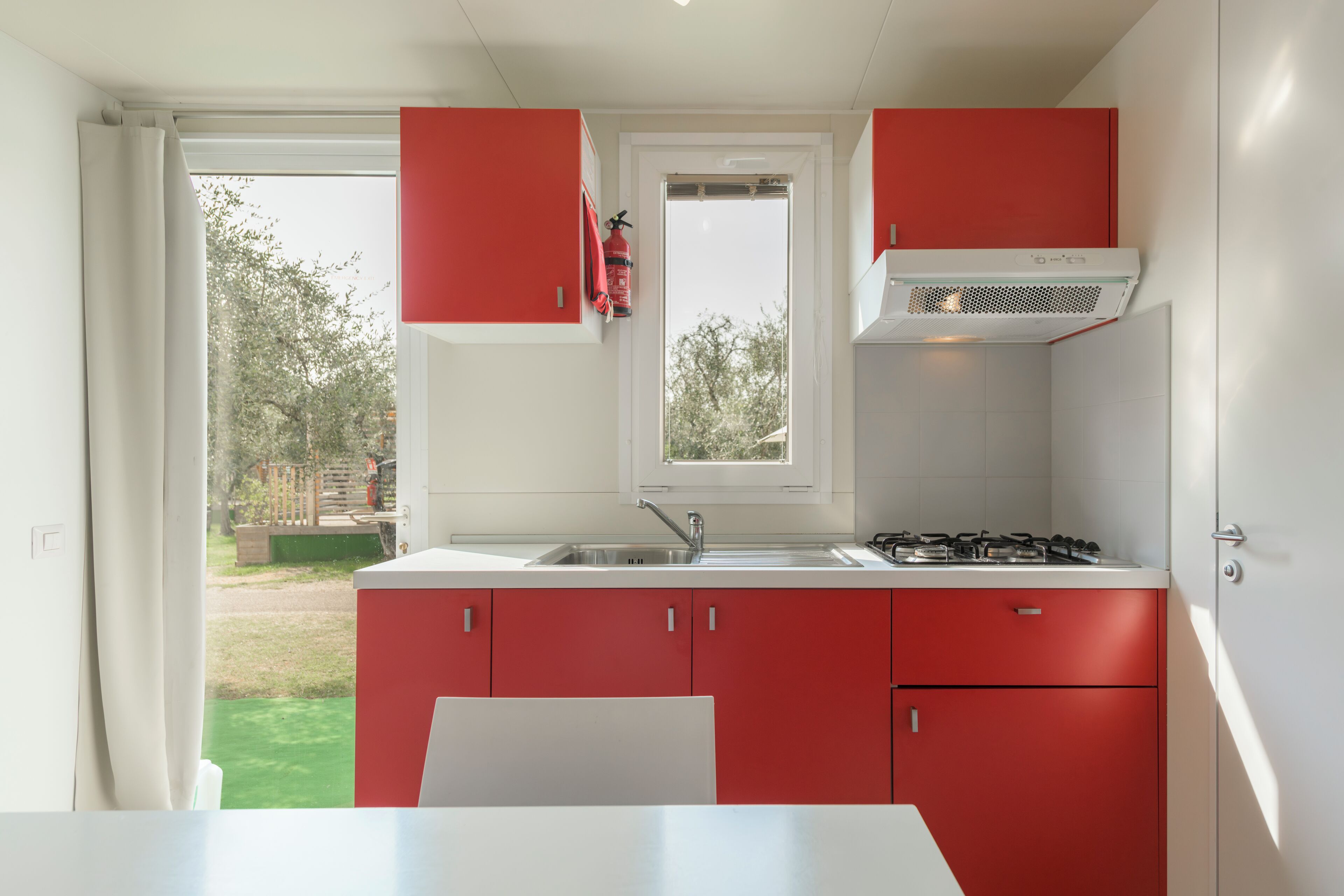 A kitchen with red cabinets, a white countertop, a gas stove, and a window with a view of the outdoors.