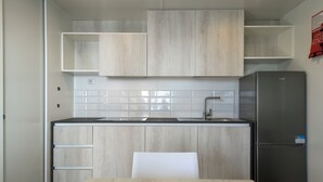 A modern kitchen with light wood cabinetry, a stainless steel refrigerator, and a white tiled backsplash. - Camping Fontanelle (Moniga del Garda)