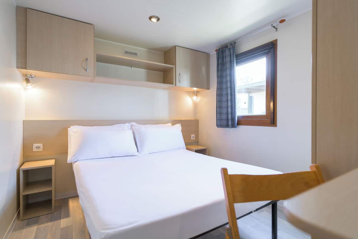 Habitación de hotel ordenada con cama, mesitas de noche, una silla y armarios empotrados de madera.