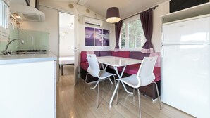 A compact kitchen with a dining area, including a white table and chairs, a built-in oven, and a refrigerator. - Camping Fontanelle (Moniga del Garda)