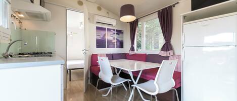 Une cuisine compacte avec un coin repas, comprenant une table et des chaises blanches, un four encastré et un réfrigérateur.