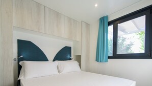 A neatly made bed with a headboard, a window with curtains, and a view of greenery outside. - Camping Fontanelle (Moniga del Garda)