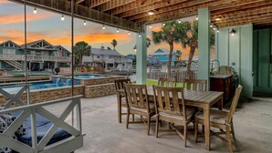 A poolside area with wooden chairs and a table, a view of houses, and a sunset. - Flamingo House 4 Bedroom Home by RedAwning (Rockport)