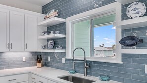 A modern kitchen with white cabinets, a stainless steel sink, and blue-tiled backsplash. - Flamingo House 4 Bedroom Home by RedAwning (Rockport)
